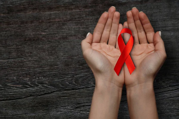 a red ribbon for the WORLD AIDS symbol is held on a wooden table