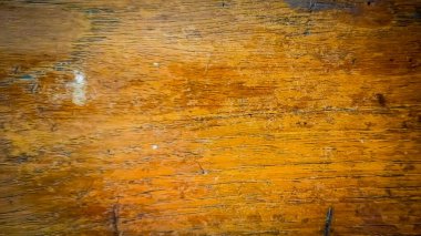 Close-up of wood surface texture with very clear wood grain, brown tones and darker streaks indicating natural pattern. There are small scratches and stains throughout the surface, indicating age or use.