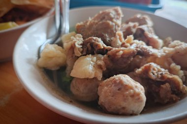 Köfteli bir kase çorba, et parçaları ve sebzeler, tahta bir masada kaşıkla servis edilir..