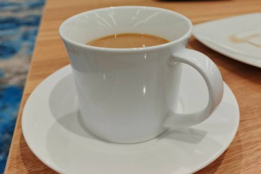 Bir fincan beyaz kahve, bir fincan çay tabağının üzerinde, ahşap bir masanın üzerinde..