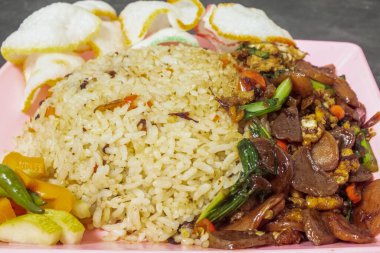 Kızarmış pirinç, kızarmış sebze, kraker ve turşu ile servis edilir..