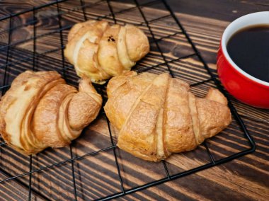 Soğutma rafında üç kruvasan, bir fincan sade kahvenin yanında..