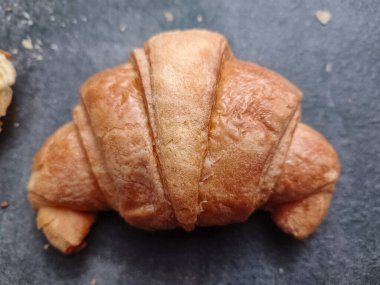 Koyu taştan bir yüzeyde altın kruvasan, gevrek ve pullu..