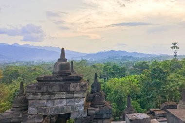 Orta Cava, Endonezya 'daki yemyeşil ormanların ve uzak dağların oluşturduğu bir zemin üzerine kurulmuş Borobudur' un ikonik budalalarının yer aldığı sakin bir manzara. Görüntü, bu antik tapınağın sükunetini ve tarihsel önemini yansıtıyor..