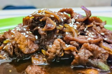 Susam tohumlarıyla kaplı, popüler bir Kore yemeği olan lezzetli bir biftek bulgogi tabağının yakın çekimi. Bu resim yemeğin zengin renklerini ve dokusunu yakalar, onu yemek pişirme ve seyahat temaları için mükemmel kılar..