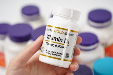 Dnipro, Ukrayna -09.09.2023: Kadın elinde bir şişe D3 vitamini. Altın, D3125 mcg vitamin. 90 sebze kapsülü. Vejetaryen gıda takviyeleri.