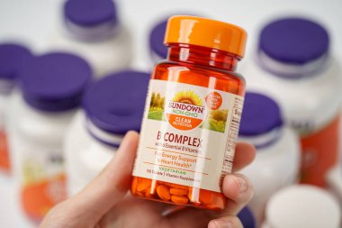 Dnipro, Ukrayna -09.09.2023: Kadın elinde SUNDOWN 'dan bir şişe B kompleksi. Günbatımı, B kompleksi 100 sebze kapsülü. Vejetaryen gıda takviyeleri.