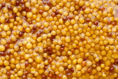 Metal kaşıkta Fransız Dijon hardalı, hardal taneciklerinin arka planda üst görünümü. Gastronomi konsepti, organik gıda. Sos. Çemberde yavaş döndürme.