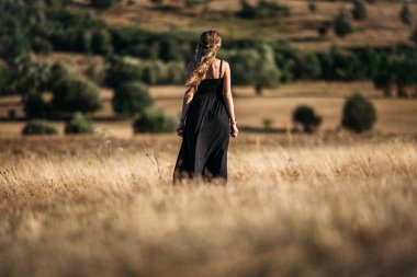Back view of a adorable young woman with long blonde hair walking in the meadow