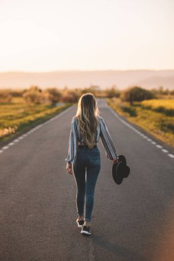Happy caucasian blonde girl walking on the road at sunset. Summer holiday concept travel, color of vintage tone and soft focus. 