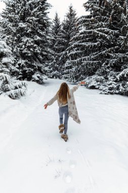 Winter walk, a young beautiful blonde in winter clothes walking in a snowy forest, a beautiful frosty day. happy woman warms a long white scarf.