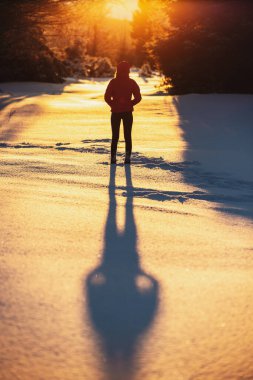 Young female standing on the snow and enjoying the sunset in the forest