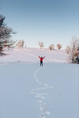 Joyful woman having fun outdoors in winter. Raised up hands on the mountain covered with snow, enjoying beautiful sunset 