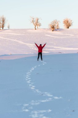 Happy joyful woman having fun outdoors in winter. Raised up hands on the mountain covered with snow, enjoying beautiful sunset