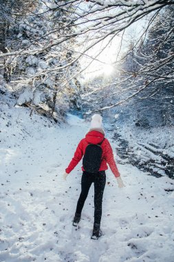 Backpacker young woman wearing red jacked and white hat. Enjoying the sunny weather outdoors after first snow in the woods. 