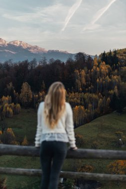 Social distancing, a young wonderful woman is standing alone and enjoying the majestic sunset in the mountains. 