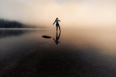 Young woman with reflection standing in the foggy lake near the wilderness forest. 