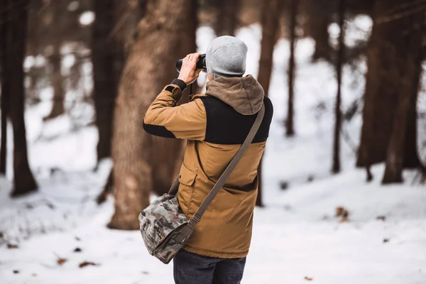 side view of man watching through binoculars in the winter forest