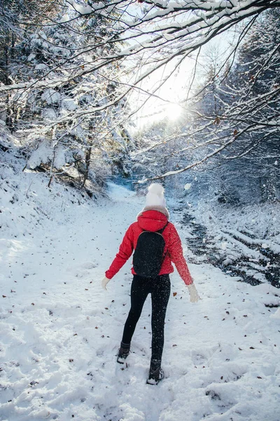Backpacker young woman wearing red jacked and white hat. Enjoying the sunny weather outdoors after first snow in the woods. 