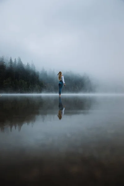 Young person standing in the foggy lake near the wilderness forest. Lifestyle, hipster style. 