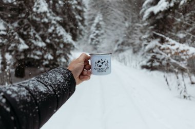 Man Holding Mug With Warm Drink In The Snowy Forest And drink hot coffee. Adventure Begins. Hiking and camping concept.  clipart