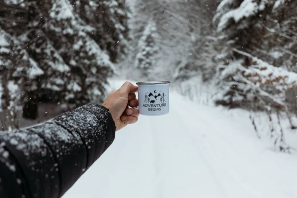 Man Holding Mug With Warm Drink In The Snowy Forest And drink hot coffee. Adventure Begins. Hiking and camping concept.