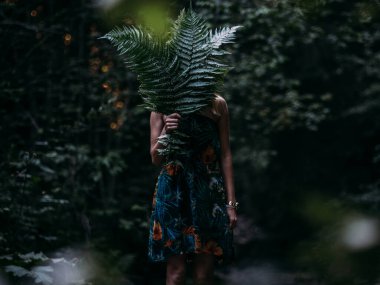 Young woman in beautiful dress holding fern leaves in forest
