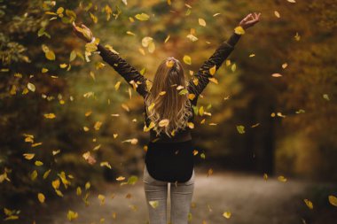 Beautiful woman cheerfully throws autumn leaves in nature 