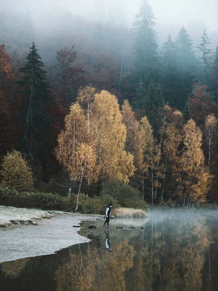 Man Traveler standing alone on pond lake and foggy mountains on background. Travel Lifestyle concept