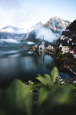 Moody view of famous beautiful old town Hallstatt and alpine deep lake in scenic foggy morning. Summer season, creative, vintage style  clipart