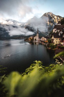 Moody view of famous beautiful old town Hallstatt and alpine deep lake in scenic foggy morning. Summer season, creative, vintage style  clipart