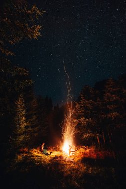 Man sitting near campfire under the stars in the wild forest. Weekend activities concept  