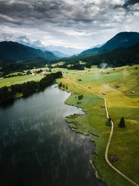 Wonderful aerial nature landscape at Bavarian alps. Dark clouds, green fields with rural road, above the lake of Gerdolsee. Germany, Europe.