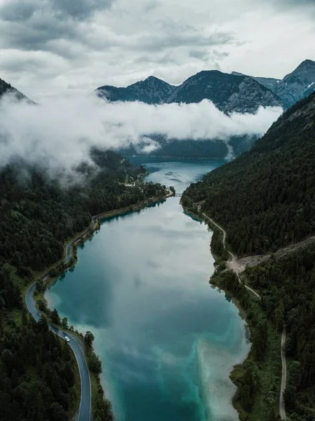 Beautiful aerial nature landscape. Azure mountain lake surrounded by evergreen pine trees in a foggy-misty day. Plansee lake, Tirol, Austria, Europe