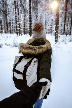 Young caucasian couple winter adventures. Hold each other hands, girl and her boyfriend walking in the forest 