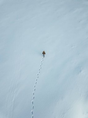 Young traveler girl walking in the deep snow, captured from above with drone
