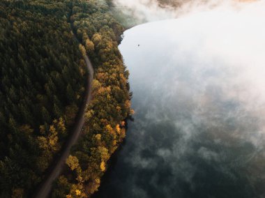 Fog covering the colorful forest and the lake in early morning landscape in autumn season. Captured from above with drone