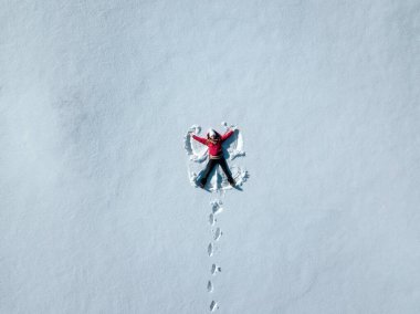 Aerial shot of woman in snow making snow angel. Woman lying in snow. copy space text.