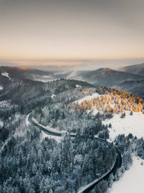 Aerial view of winding road from high mountain pass with snow covered trees in Transylvania, Romania. Nature travel concept.