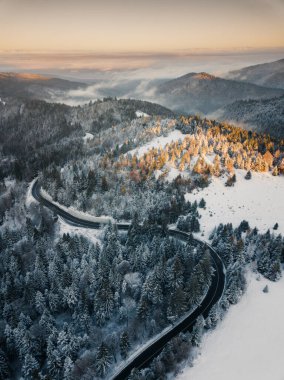 Aerial view of winding road from high mountain pass with snow covered trees in Transylvania, Romania. Nature travel concept.