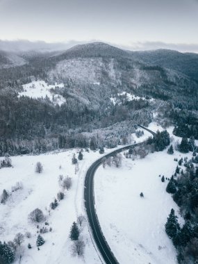 Aerial view of winding road from high mountain pass with snow covered trees in Transylvania, Romania. Nature travel concept.