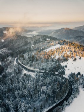 Aerial view of winding road from high mountain pass with snow covered trees in Transylvania, Romania. Nature travel concept.