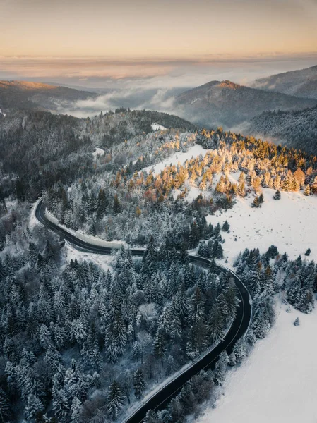 Aerial view of winding road from high mountain pass with snow covered trees in Transylvania, Romania. Nature travel concept.
