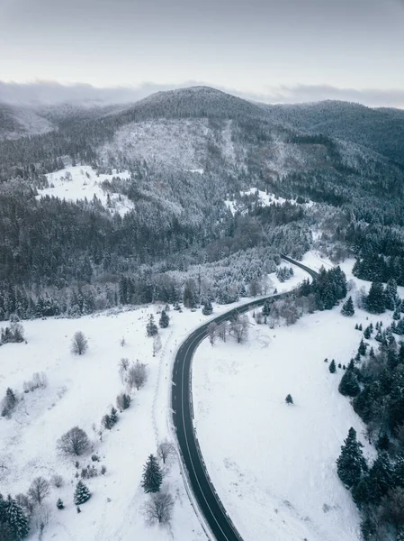 Aerial view of winding road from high mountain pass with snow covered trees in Transylvania, Romania. Nature travel concept.