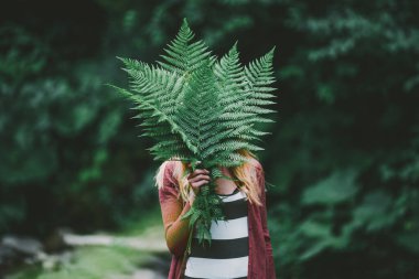 Young woman in beautiful dress holding fern leaves in forest