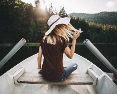 Şapkalı güzel sarışın kadın kayıkta oturuyor.