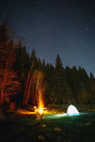 Illuminated tent and campfire under beautiful night sky full of stars in the wild forest