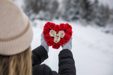 Young woman holding a bouquet of red and white roses in the shape of a heart in the winter  forest. Romantic Valentine's Day concept.