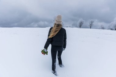 Young hiker woman  in a black jacket with a bouquet of flowers in her hands walks in the snow. 