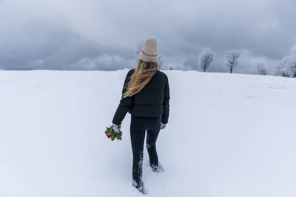 Young hiker woman  in a black jacket with a bouquet of flowers in her hands walks in the snow.